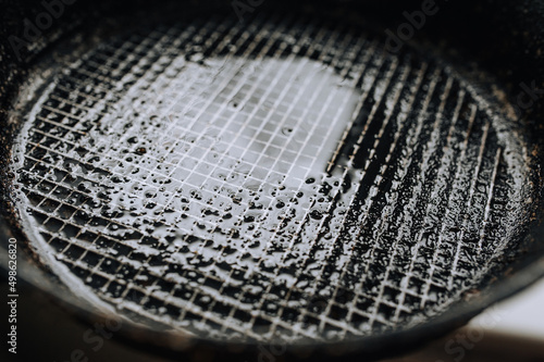 Background, texture, top view of a black round frying pan with a checkered pattern, after cooking, smeared with sunflower, olive oil. Photo of dirty, old dishes. © shchus