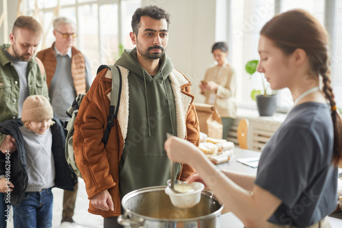 Valokuvatapetti Portrait of young man standing in line at soup kitchen with young woman giving o