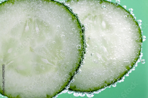 Cucumbers sliced in water with bubbles close up image on green background.