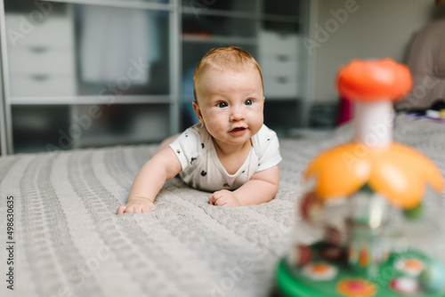 Portrait of a baby crawling to toys on bed in the room. Adorable baby boy in bedroom. Newborn child playing. Nursery for children. Family morning at home.