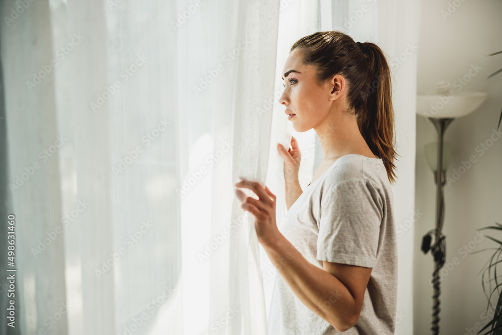 Woman Feeling Worried While Standing Near The Window At Home Woman Feeling Worried While Standing Near The Window At Home
