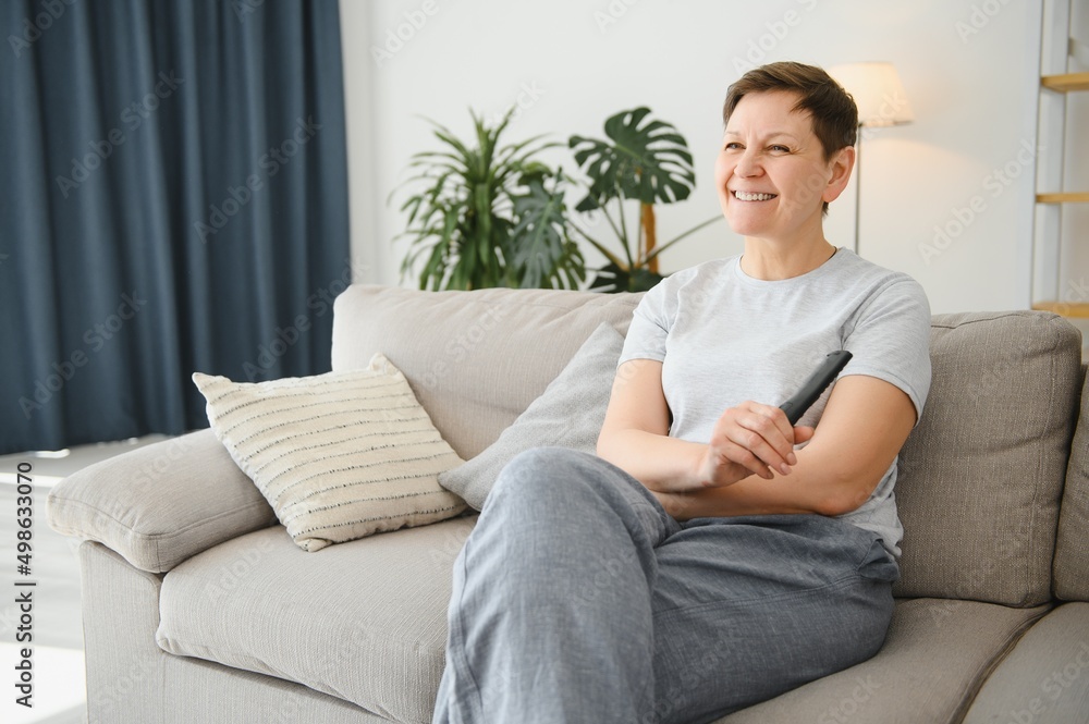 Woman sitting in living room holding remote control smiling. Woman sitting in living room holding remote control smiling.