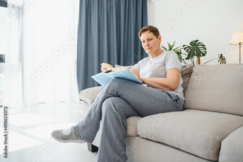 Attractive middle-aged woman with a lovely smile sitting on a sofa in the living room clutching a book.