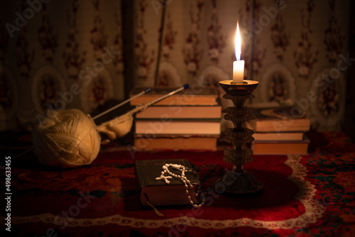Still life with rosary on the prayer book, candle in vintage old candlestick and books near the window. Vintage old tablecloth on the table. Christianity concept. Time of prayer.