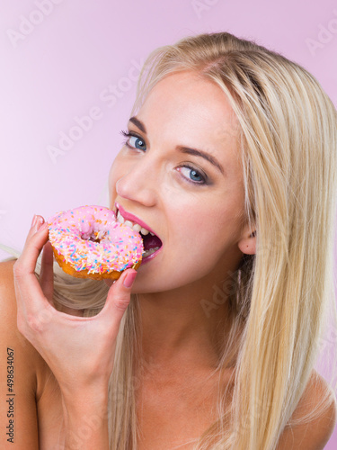 Mmm..who says I cant indulge. Cropped shot of a woman eating a donut while isolated on pink.