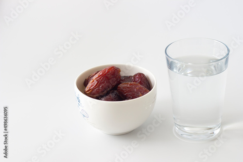Date berries in a white bowl with a glass of water next to it. Isolated on white background. To break the fast in Ramadan