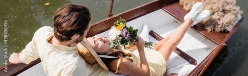 high angle view of young woman in straw hat holding bouquet of flowers and lying in boat with man, banner.