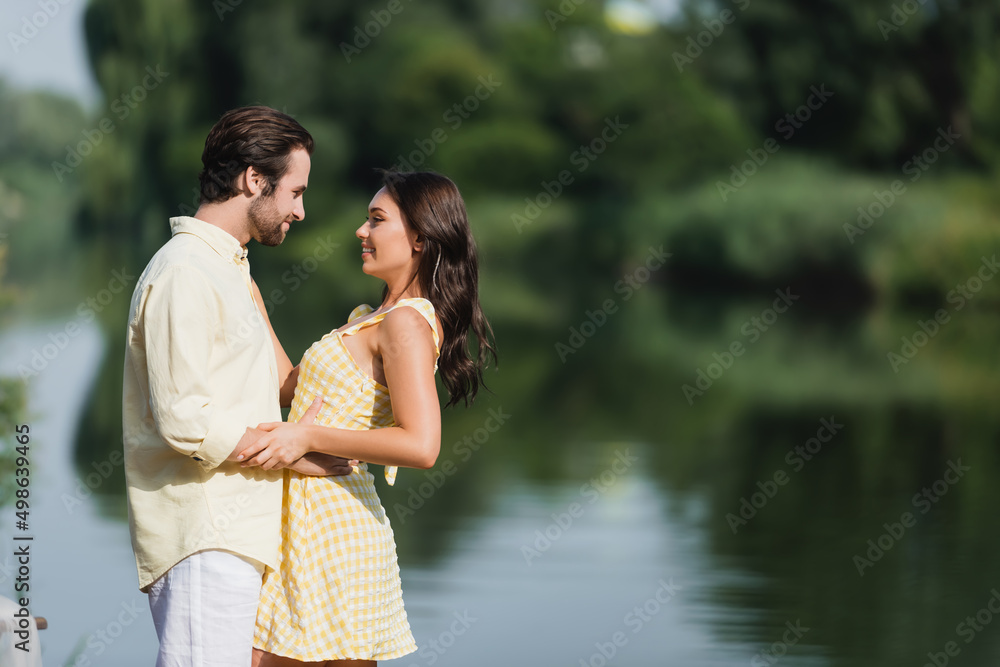 side view of pleased young couple looking at each other near lake.