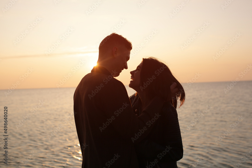 Silhouette of young happy smiling couple hugging over sunset background on the sea beach.