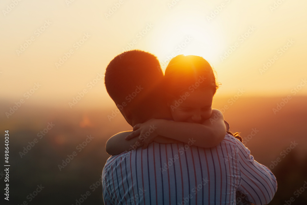 The little cute daughter hugs his father in nature at sunset. Amazing sunset, close up.