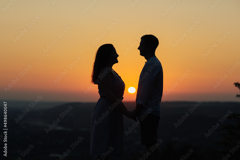 Silhouette of young couple holding hands and looking at each other on a date at amazing orange sunset.