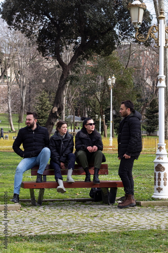 Obraz premium Four young people sitting on bench and talking each others. Friendship, fun and joy concept.