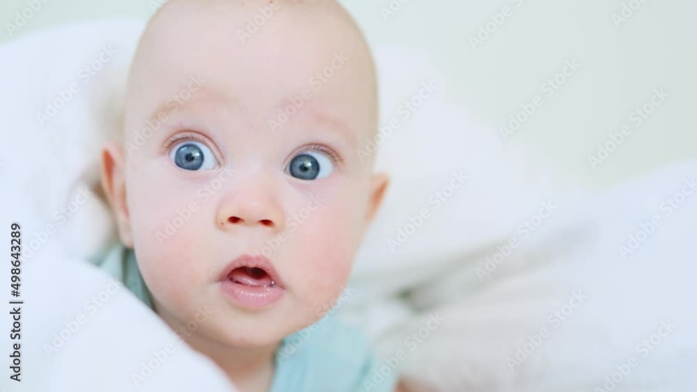 beautiful blue eyed infant baby portrait close-up, smiling face of little child lying in white bed on stomach. happy caucasian toddler baby portrait, funny kid looking camera opening mouth, emotions beautiful blue eyed infant baby portrait close-up, smiling face of little child lying in white bed on stomach. happy caucasian toddler baby portrait, funny kid looking camera opening mouth, emotions