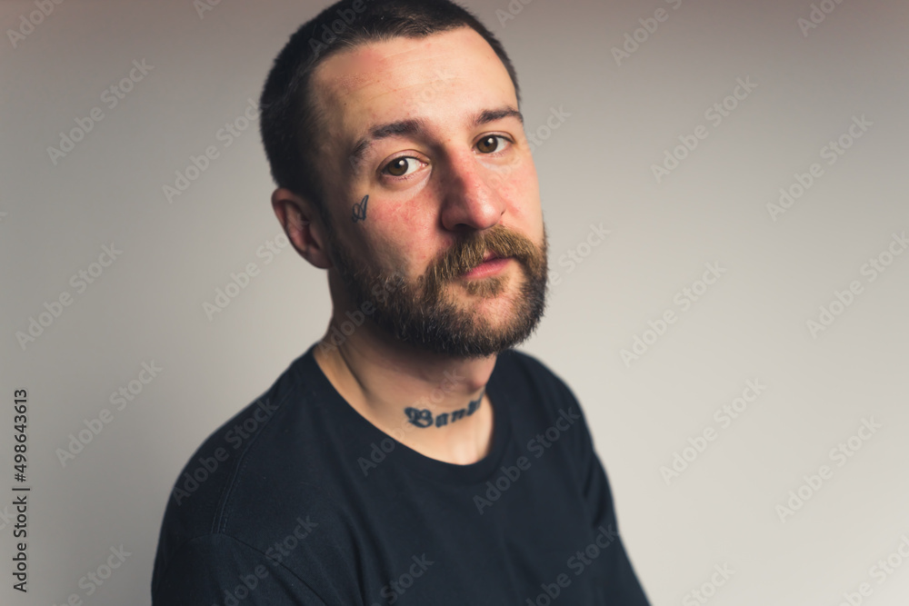 handsome bearded tattooed European young man with a mustache looking seriously medium closeup gradient background studio shot. High quality photo