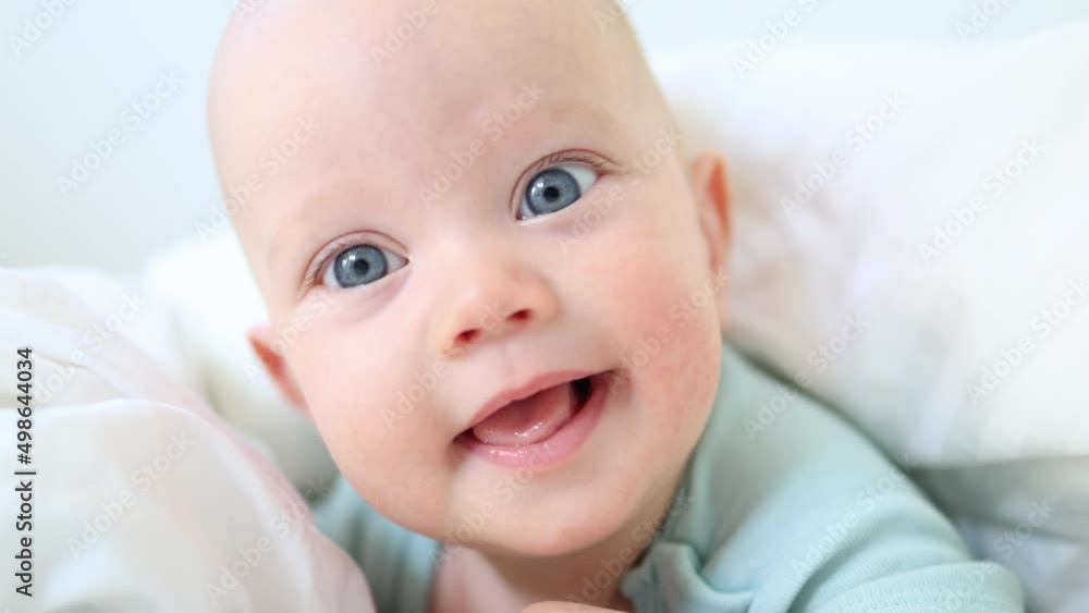 beautiful blue eyed infant baby portrait close-up, smiling face of little child lying in white bed on stomach. happy caucasian toddler baby portrait, funny kid looking camera opening mouth, emotions beautiful blue eyed infant baby portrait close-up, smiling face of little child lying in white bed on stomach. happy caucasian toddler baby portrait, funny kid looking camera opening mouth, emotions