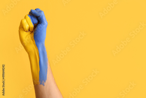 Man with clenched fist painted in colors of Ukrainian flag on yellow background