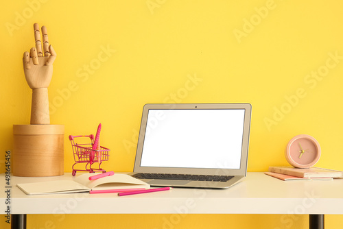 Modern laptop and stationery supplies on table near color wall