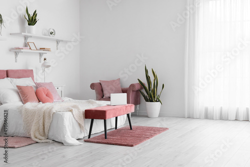 Interior of stylish bedroom with soft ottoman and houseplant