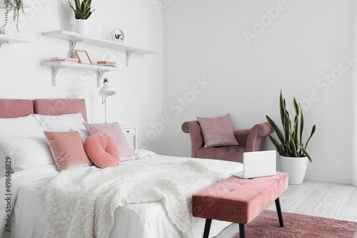 Interior of stylish bedroom with soft ottoman and houseplant