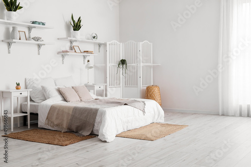 Interior of stylish bedroom with nightstands, folding screen, houseplants and lamp