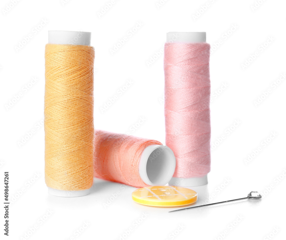 Thread spools, ball pin and button on white background
