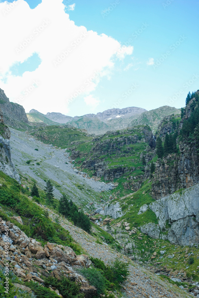 Green valley surrounded by mountains and a clear blue sky with some clouds