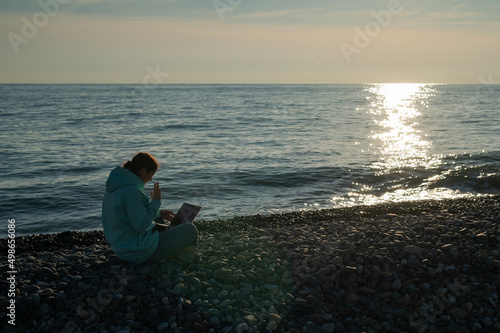 Caucasian woman communicating by video call on laptop on pebble beach.  © Михаил Решетников