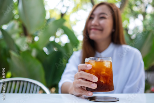 Portrait image a young asian woman holding and drinking iced coffee in the outdoors cafe
