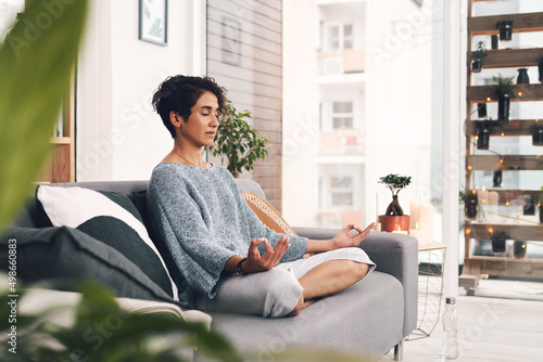 I didnt choose the zen life, it chose me. Full length shot of an attractive young woman sitting and meditating on her sofa in the living room at home.