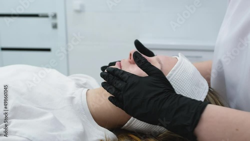 Cosmetologist applies a woman a therapeutic mask on her face. Woman in a spa salon on cosmetic procedures for facial care. Beautician makes a massage of the face with a moisturizing mask on a face.