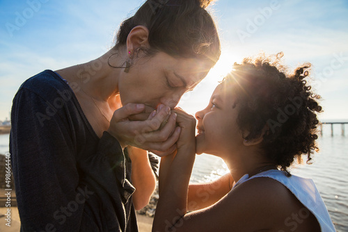 Foto Caucasian mother kissing her african adopted daughter hands sharing a deep and lovely moment together outdoors at sunset time during summer vacation