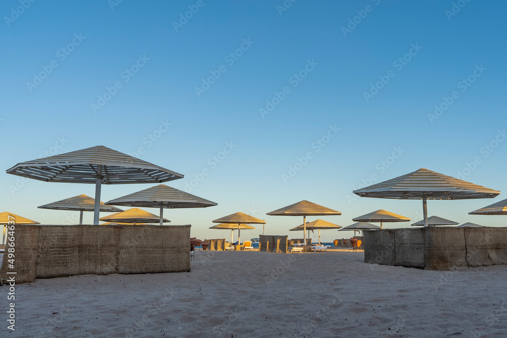 A clear morning on the Red Sea coast. Lattice sun umbrellas and wicker fences stand on the sandy beach. Blue sky. Egypt. Safaga