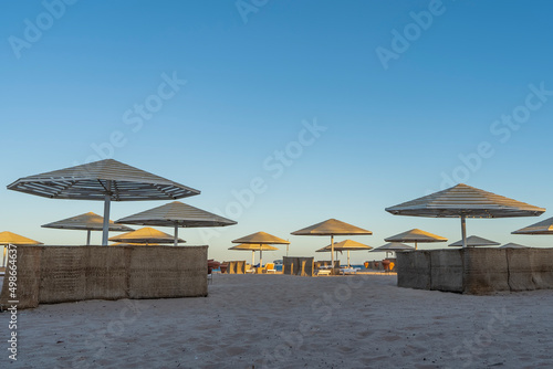 A clear morning on the Red Sea coast. Lattice sun umbrellas and wicker fences stand on the sandy beach. Blue sky. Egypt. Safaga