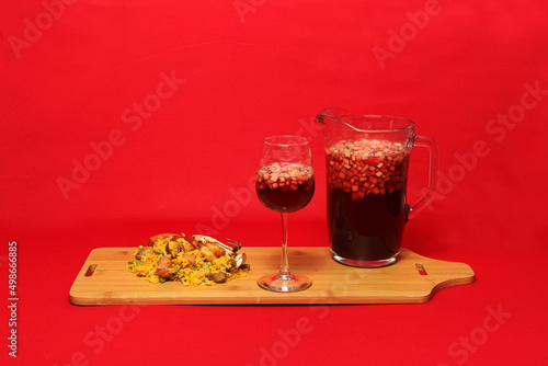 Paella rice with seafood traditional dish from Valencia Spain served on a white plate next to a pitcher of clericot with fruits and a crystal glass on a red background
 photo