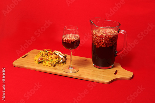 Paella rice with seafood traditional dish from Valencia Spain served on a white plate next to a pitcher of clericot with fruits and a crystal glass on a red background 