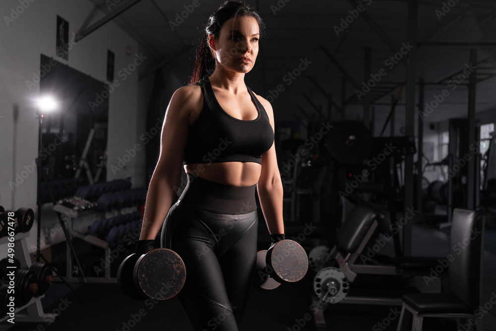 Determined woman loses weight in the gym and trains with dumbbells. concept of sports and recreation. Beautiful woman in sportswear with heavy dumbbells in her hands. Determined woman loses weight in the gym and trains with dumbbells. concept of sports and recreation. Beautiful woman in sportswear with heavy dumbbells in her hands.