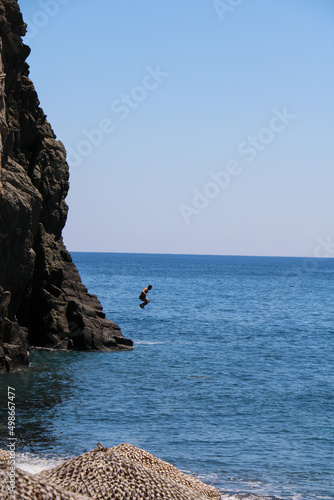 Caucasian male jumping from a cliff into the blue sea. Clear Blue skies.