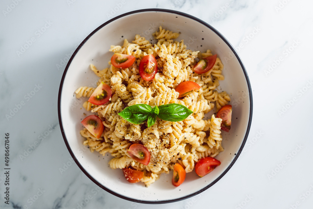 creamy vegan garlic fusilli pasta with cherry tomatoes and basil topping, healthy plant-based food