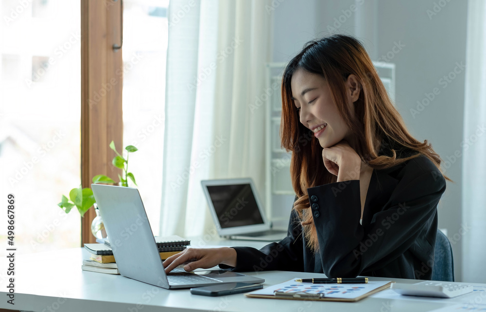 Happy young asian businesswoman sitting on her workplace in the office. Young woman working at laptop in the office. Happy young asian businesswoman sitting on her workplace in the office. Young woman working at laptop in the office.