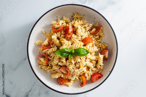 creamy vegan garlic fusilli pasta with cherry tomatoes and basil topping, healthy plant-based food