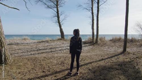 Young healthy fitness woman taking exercise break looking over the horizon and beach from a glade among trees. Different poses, blue sky and sunny weather. Static wide angle shot. photo