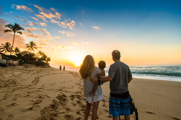 Young family watching a beautiful ocean sunset together at  Sunset Beach, Oahu, Hawaii. Beautiful scenic view on a Hawaiian beach. Family moments together