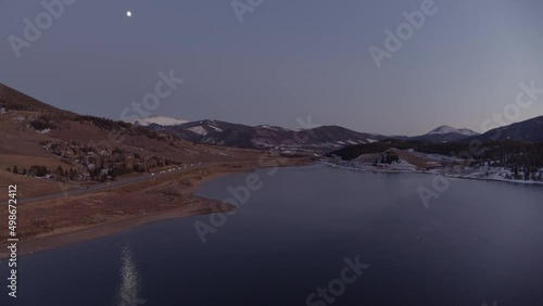 drone shot of a lake in the mountains with the full moon reflecting off the water on a cold winter night