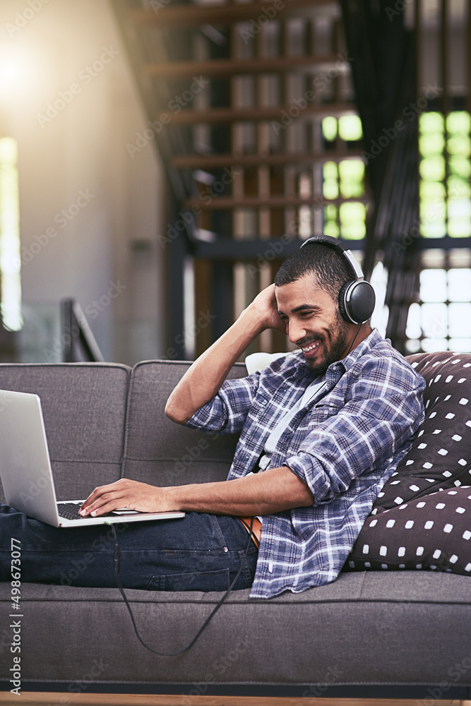 Thats my jam. Shot of a young man using a laptop and headphones on the sofa at home. Thats my jam. Shot of a young man using a laptop and headphones on the sofa at home.
