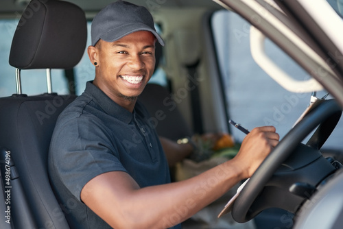 Going on his delivery rounds. Portrait of a courier writing on a clipboard while sitting in his van.