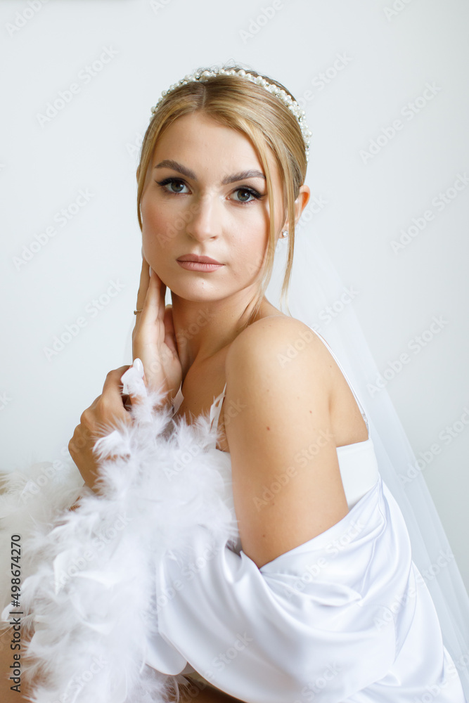 Gorgeous beautiful bride in silk robe posing near window in soft light in the morning. Gorgeous beautiful bride in silk robe posing near window in soft light in the morning.
