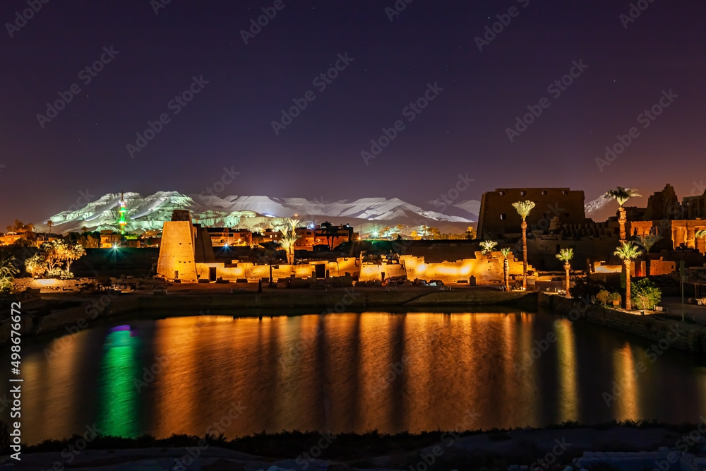 Night scene of Karnak Temple Complex in Luxor with a sacred lake and the ruined structure.