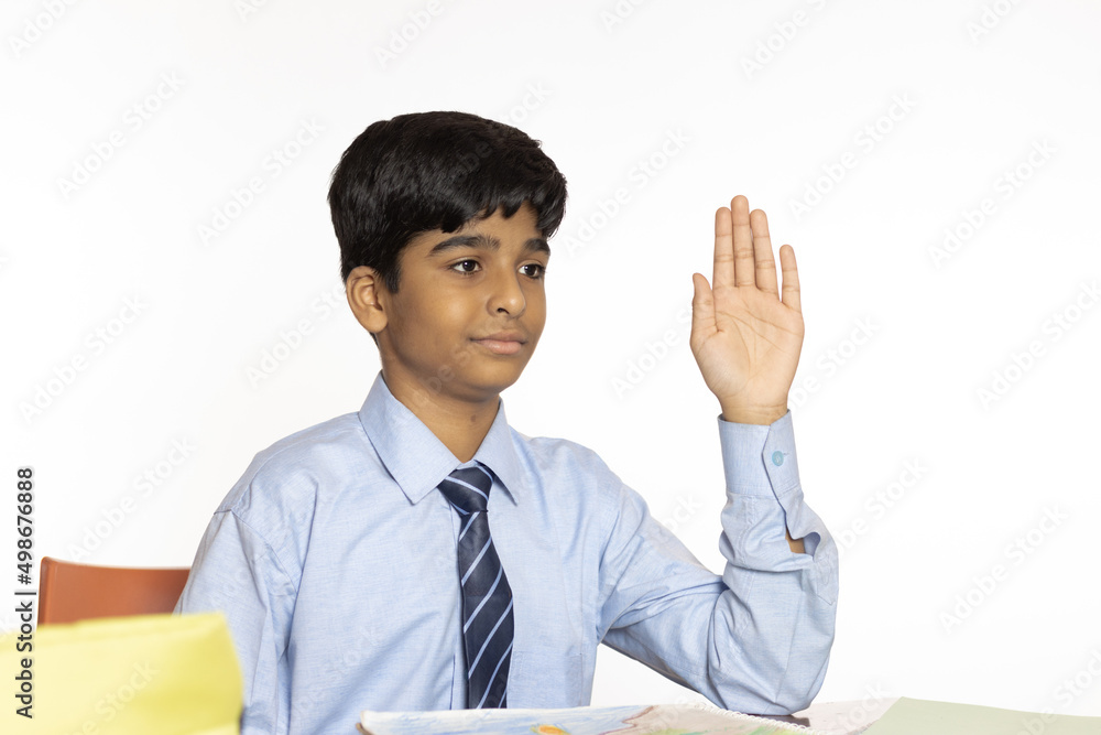 young boy of primary school sitting in classroom raising hand to respond to a question isolated on white background young boy of primary school sitting in classroom raising hand to respond to a question isolated on white background