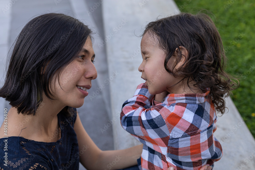Mom and her Latin American son sitting on a bench showing their love with smiles and happiness. Mother's day concept and family Mom and her Latin American son sitting on a bench showing their love with smiles and happiness. Mother's day concept and family