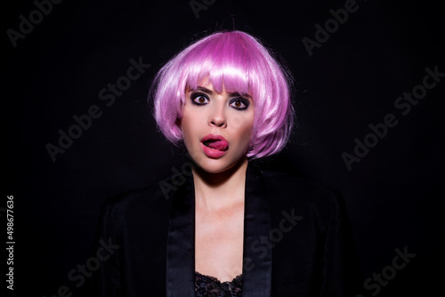 Funny woung woman tongue lick lips. Close-up portrait of amazing female model in pink wig. Studio photo funny surprised humoured girl in wigs. Emotional woman portrait. photo